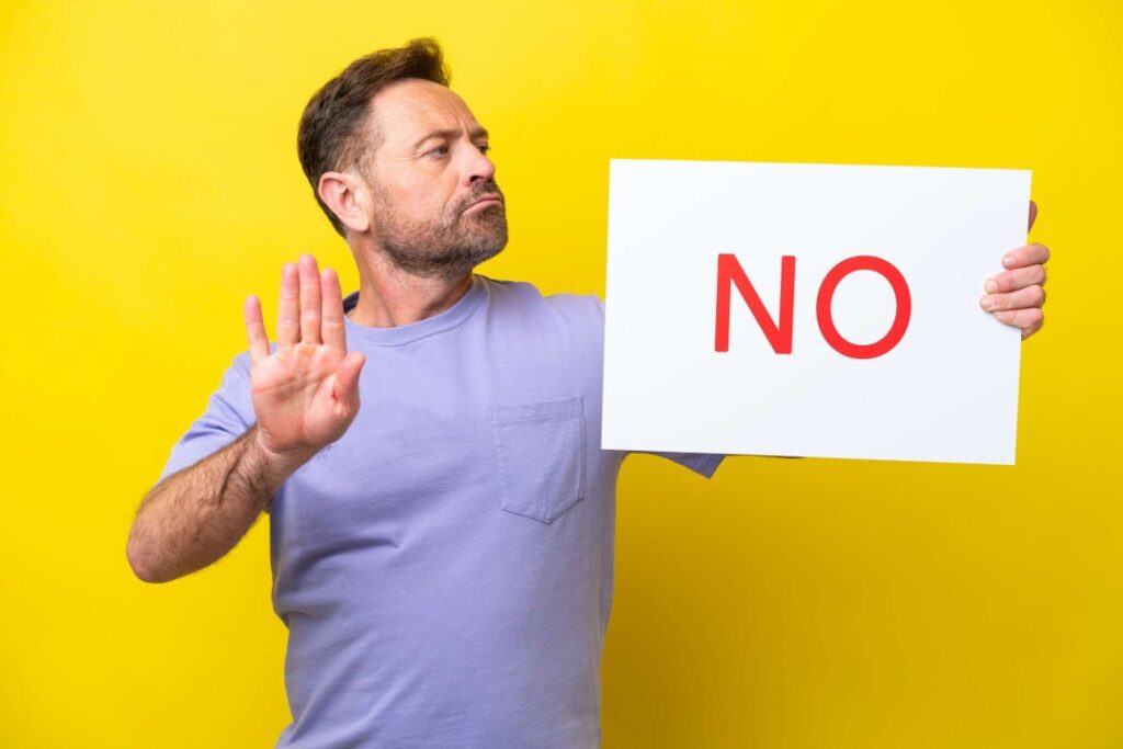 Man holding up a red no sign on yellow background.