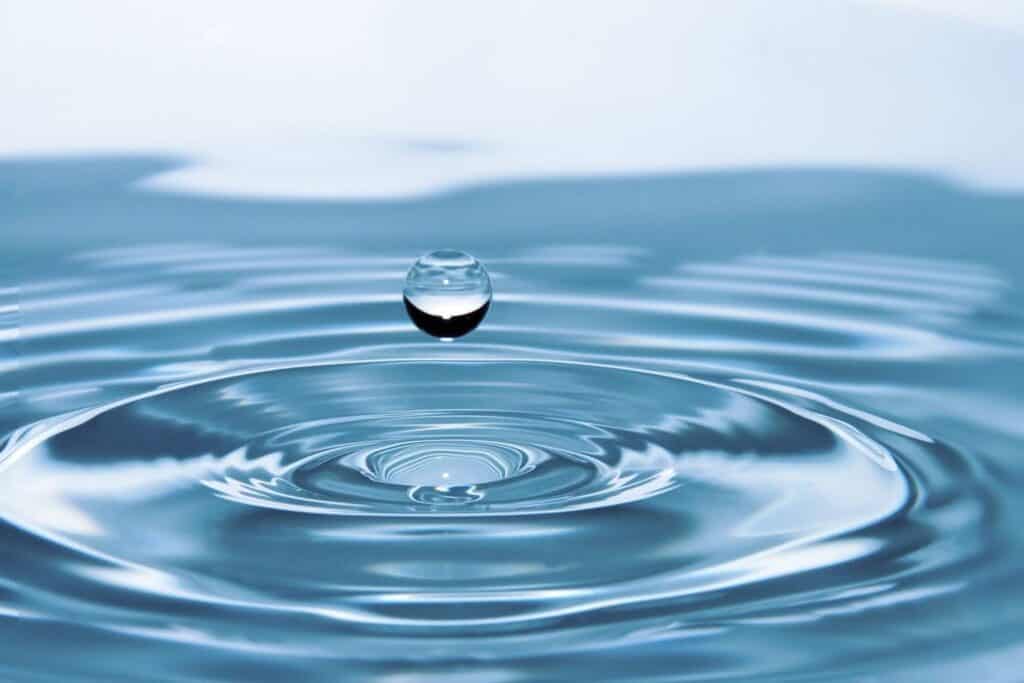A single water drop rests on a smooth blue surface, reflecting light and creating a serene visual effect signifying the power of self-belief with SATORI ATTITUDE.